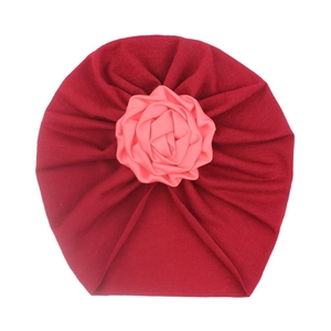 Detail of baby turban featuring a large pink satin flower on dark red knit fabric