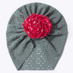 Détail du bonnet en dentelle ajourée pour bébé avec une grande rose rouge dessus