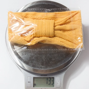 Detail shot of bright yellow knitted baby headband on a scale showing 13.3g weight