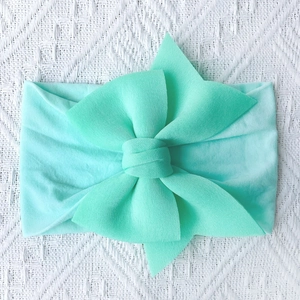 Close-up of mint green baby headband with a soft nylon bow on a white lace background
