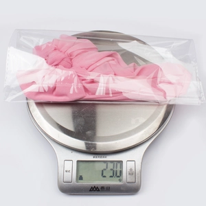 Pink soft mesh baby turban hat with bow knot design being weighed on a digital scale