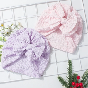 Pink and purple soft textured baby turban hats with large decorative bow on white grid