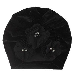 Détail d'un turban pour bébé en velours noir avec des fleurs artisanales et des strass
