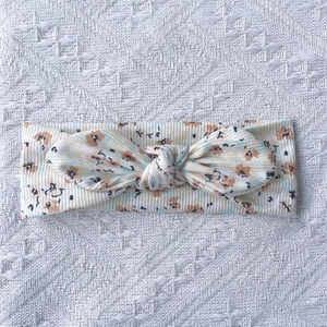 Détail d'un bandeau bébé en maille côtelée à fleurs avec nœud sur fond de dentelle blanche
