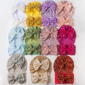Flat lay of ribbed baby turban and headband set with gold polka dot bow in various colors