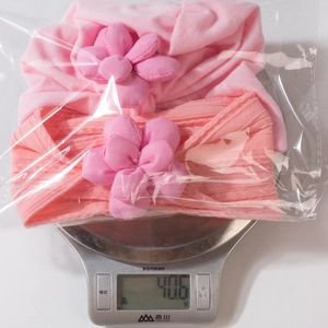 Detail showing baby flower headbands in packaging being weighed at 40.6 grams