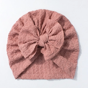 Detail of baby turban hat featuring a large bow and soft ribbed texture in Morandi pink