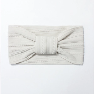Detail of soft cream white cable-knit baby headband with elastic bow design