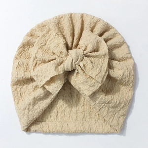 Detailed view of soft cream baby turban hat with ribbed texture and large bow decoration