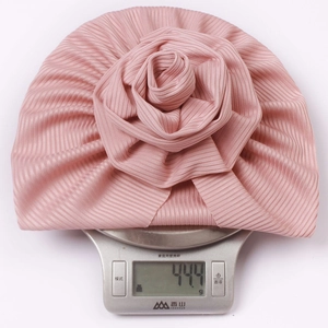 Close-up of pink ribbed baby turban hat with rose decoration showing weight on scale