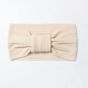 Detail of a creamy white knitted baby headband featuring a bow knot and ribbed texture