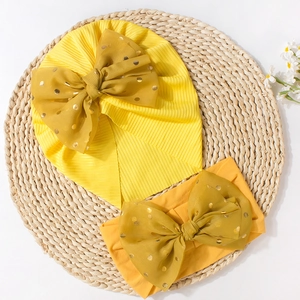 Detail of yellow ribbed baby hat and headband set with gold-dot tulle bow on woven mat
