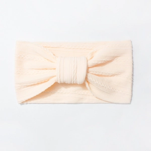 Close-up of cream beige cable knit baby headband with large bow detail and soft texture