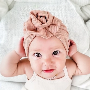 Detail of baby ribbed knit turban hat with large decorative rose in dusty pink color