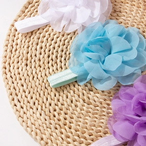 Three chiffon flower baby headbands in white, blue and purple on a woven mat