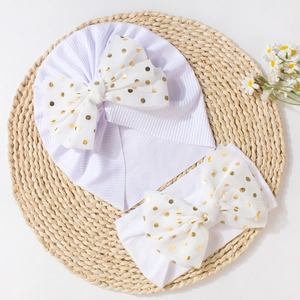 Detail of white newborn turban hat and headband with gold polka dot bow on straw mat