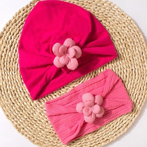 Detail view of pink baby turban hat and floral headband set on a woven texture