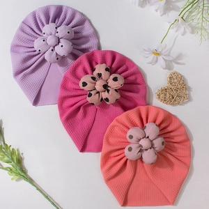 Three colorful baby turban hats with floral details in lavender, rose, and coral pink