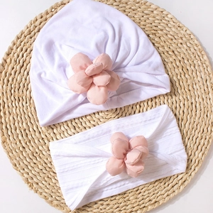Close-up of white baby beanie and headband set with 3D pink fabric flower details