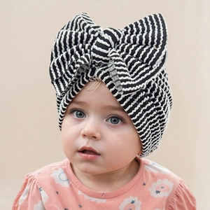 Close-up of baby girl wearing a soft black and white striped turban hat with a large bow
