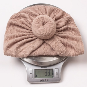 Detail showing soft jacquard knit infant hat with donut knot weighing 33.1g on scale