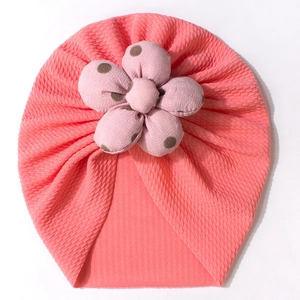 Infant turban hat in coral pink with a large polka dot fabric flower on white background