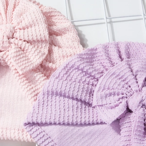 Close-up of pink and purple newborn bow hats in textured knit fabric for babies