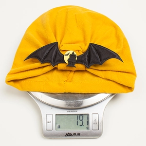 Detailed view of yellow Halloween baby turban with bat wings on a digital scale weighing 19.1g