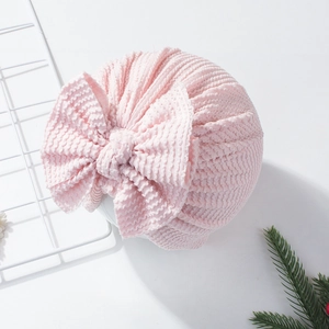 Detail of soft light pink newborn turban hat featuring a large bow and waffle knit texture