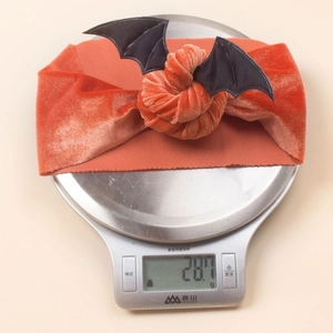Close-up of orange velvet Halloween bat headband on a digital scale weighing 28.7g