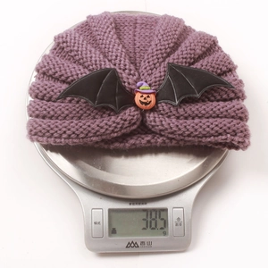 Detail of a purple knitted Halloween baby hat with pumpkin and bat wings on a scale