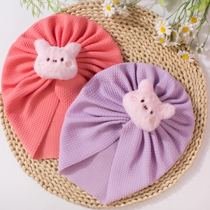 Detail of pink and purple baby hats featuring plush 3D pig decorations on knit fabric