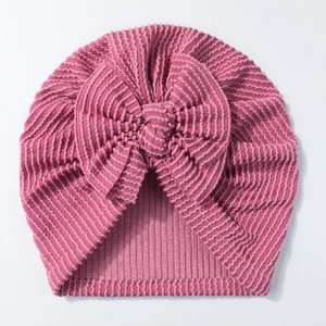Close-up of ribbed rose pink newborn hat with large decorative bow on white background
