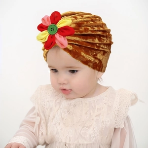 Détail d'un bonnet turban bébé en velours doré avec fleur 3D et bouton vert