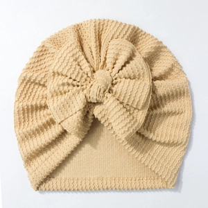 Close-up of baby beanie with a large bow and ribbed knit texture in beige color