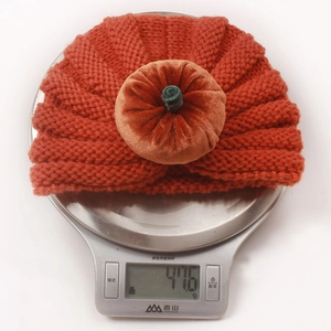 Detail showing the 47.6g weight of a knitted orange pumpkin hat on a digital scale