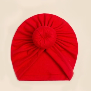 Detail einer roten Baby-Turbanmütze aus weichem Strick mit dekorativem Donut-Knoten