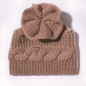 Détail d'un bonnet en tricot marron pour bébé avec torsades et fleur décorative