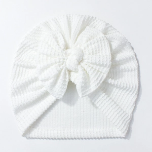 Detail of white newborn baby hat with waffle texture fabric and a large sweet bow