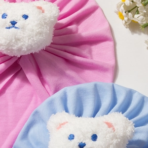 Detailed view of soft pleated baby beanies in pink and blue with plush bear decorations