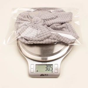 Détail du bonnet turban bébé gris en maille gaufrée pesé sur une balance sous emballage