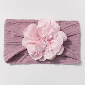 Détail d'un bandeau bébé avec une grande fleur rose clair sur un tissu tricoté violet