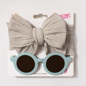 Macro detail of beige knit bow headband and light blue round sunglasses on summer display card