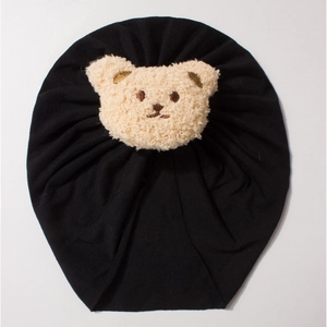 Detail of baby knot turban hat in black soft knit cotton with a beige plush bear patch