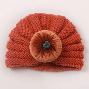 Close-up of orange knitted pumpkin baby turban with velvet knot and green stem detail