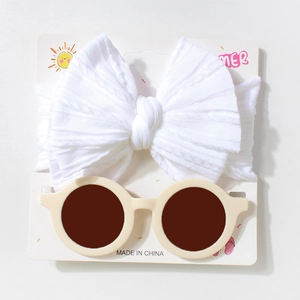 Detail of white knit bow headband and beige round baby sunglasses on display card