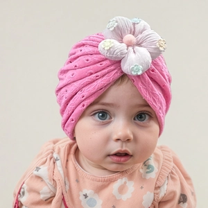 Detail of pink knit baby turban hat with a large 3D purple flower and embroidery texture