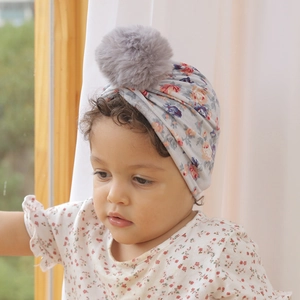 Gros plan d'un turban pour bébé à fleurs avec un pompon en fausse fourrure grise douce