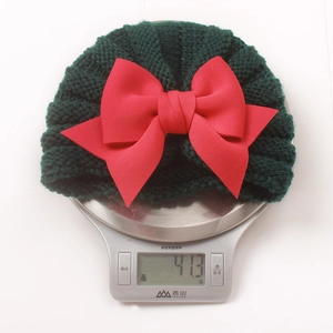 Détail d'un bonnet tricoté vert foncé pour bébé avec un grand nœud rouge sur une balance