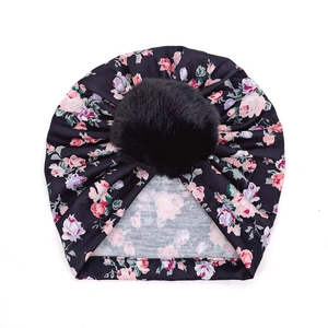 Détail d'un bonnet turban bébé à fleurs avec pompon noir en fausse fourrure douce